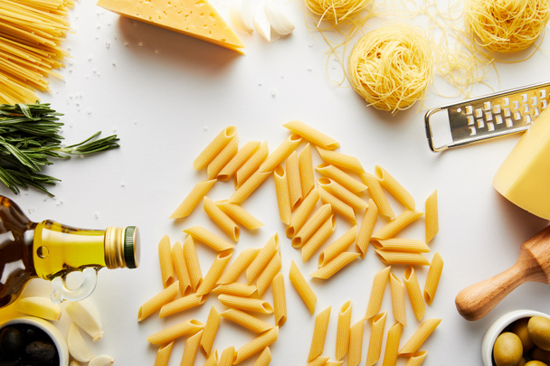 Top view of pasta, rolling pin, grater, bottle of olive oil and ingredients on white  - Zdjęcie, obraz