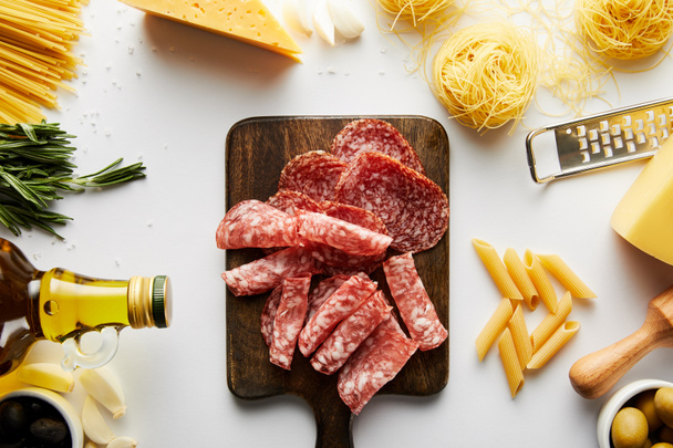 Top näkymä lihatarjotin, pasta, pullo oliiviöljyä, raastin ja ainesosat valkoisella pohjalla
  - Valokuva, kuva