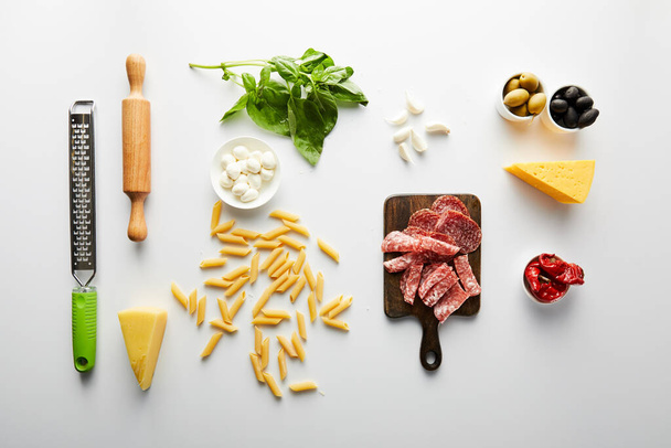Acostado plano con plato de carne, botella de aceite de oliva, rodillo, rallador e ingredientes en blanco
  - Foto, imagen