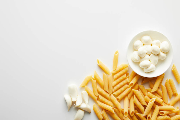 Top view of garlic, pasta and bowl with mozzarella on white background  - Photo, Image
