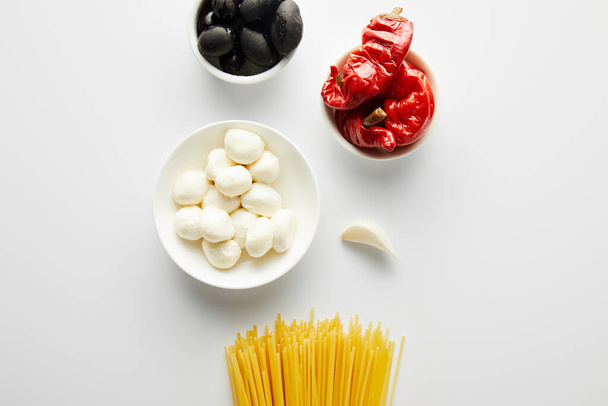 Draufsicht auf Spaghetti, Knoblauch und Schalen mit Zutaten auf weißem Hintergrund  - Foto, Bild