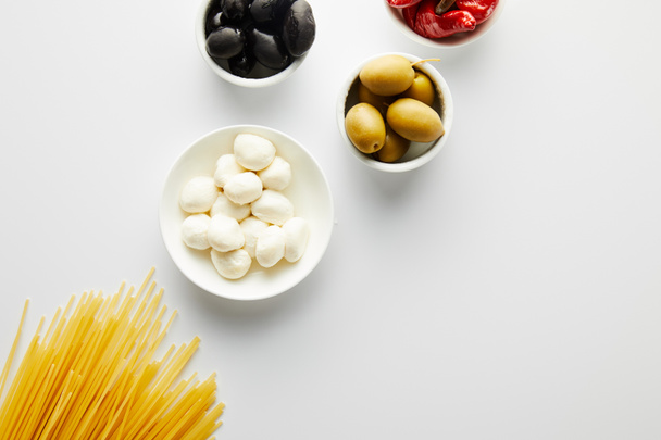 Top view of spaghetti and bowls with ingredients on white background  - Foto, afbeelding