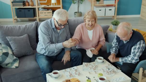 Slow motion of pensioners playing lotto game in apartment talking having fun - Materiał filmowy, wideo
