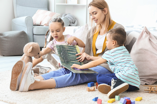 Niñera y niños pequeños y lindos leyendo libro en casa
 - Foto, imagen