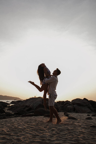a young couple in love on the beach by the sea, a girl and a man hugging at sunset - Fotografie, Obrázek