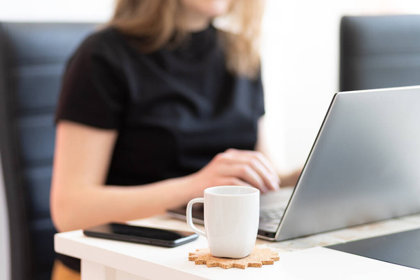 Молодая женщина, работающая за рабочим столом с документами и ноутбуком с чашкой кофе на столе
 - Фото, изображение