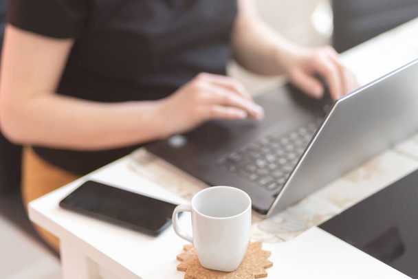 Jonge vrouw werkt aan haar bureau met documenten en laptop met een kopje koffie op tafel - Foto, afbeelding
