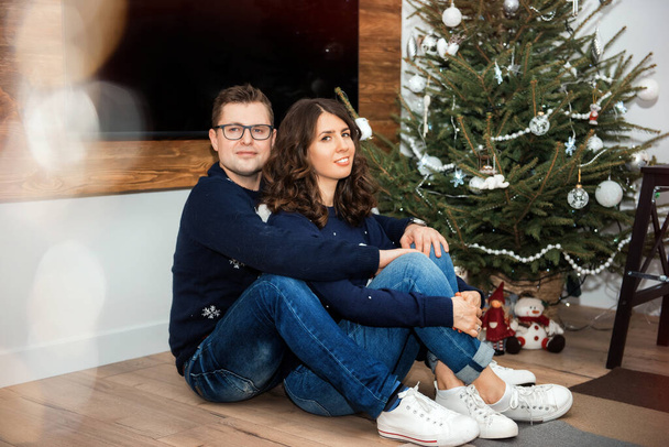 Onnellinen valkoihoinen pari istuu lähellä joulukuusi äskettäin ostettu vuokra-asunto. Pariskunta tai avioliitto uudessa kodissaan. Rakkaus, luottamus, yhdessäolo jouluna ja uutena vuotena. Rakkaus perheessä
 - Valokuva, kuva