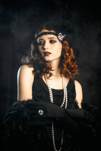 Portrait of old-fashioned red haired woman dressed in style of Great Gatsby era flirting and posing on burgundy velours background. Vintage, flapper party, retro fashion concept - Photo, Image