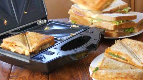 Morning breakfast in the home kitchen. Sandwiches with bacon, cheddar cheese and lettuce are fried in a special toaster or a sandwich maker. Special kitchen spatula takes fresh sandwich bread - Footage, Video
