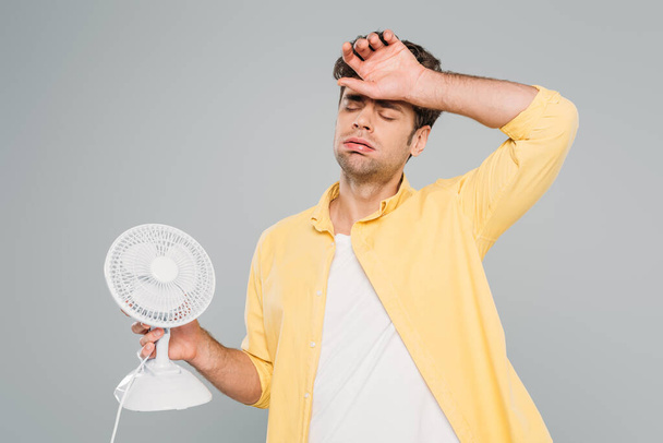 Человек с настольным вентилятором страдает от тепла, изолированного на сером
 - Фото, изображение