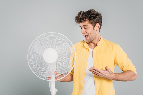Man with open mouth pointing at electric fan isolated on grey - Foto, immagini