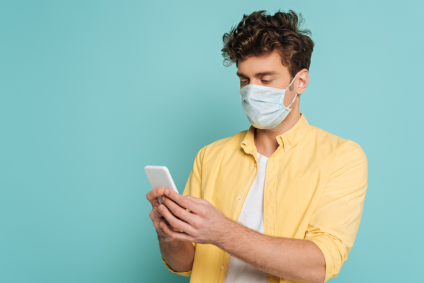 Hombre concentrado en la escritura de la máscara médica en el teléfono inteligente aislado en azul
 - Foto, imagen