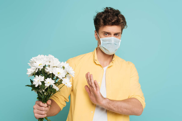 Man in medical mask with outstretched hand holding bouquet and showing no sign isolated on blue - Photo, Image