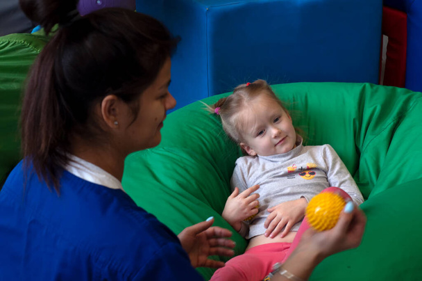 sensory therapist massaging little girl patient with a little ball - Photo, image