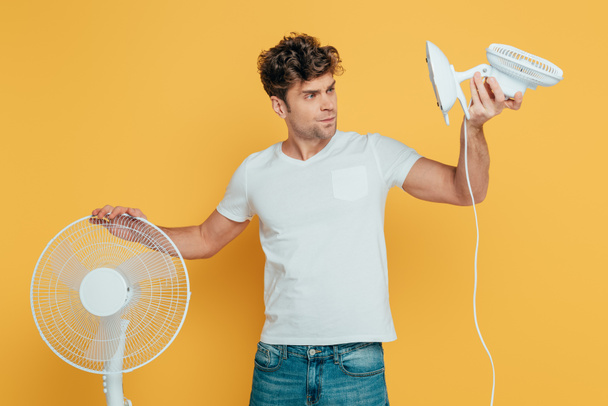 Concentrated and worried man looking at desk fan isolated on yellow - Foto, Imagem