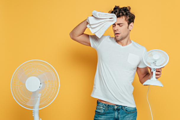 Man with towel, electric and desk fans suffering from heat on yellow - Photo, image
