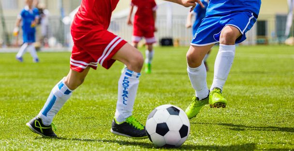 少年サッカーゲーム。ボールの後に走る子供たち。ジュニアレベルのサッカートーナメントは屋外と一致します。赤と青のジャージーシャツの選手の間の競争 - 写真・画像