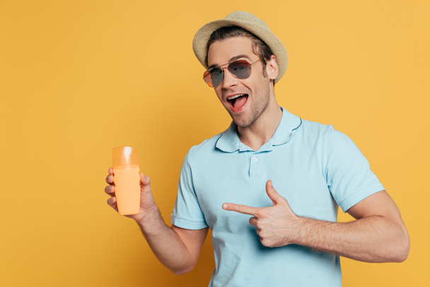 Homme excité avec bouche ouverte pointant vers une bouteille de crème solaire isolée sur jaune
  - Photo, image