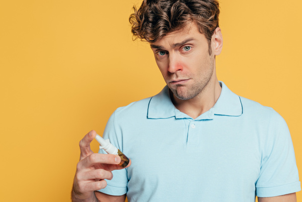 Kranker Mann mit Flasche Nasentropfen und Blick in Kamera isoliert auf gelb - Foto, Bild