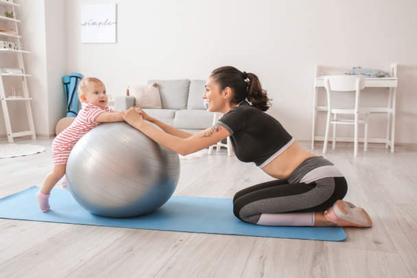 Junge sportliche Mutter und ihr Baby bei Übungen mit Fitball zu Hause - Foto, Bild
