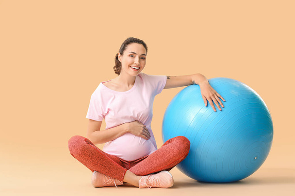 Молода вагітна жінка робить вправи з фітболом на кольоровому фоні
 - Фото, зображення