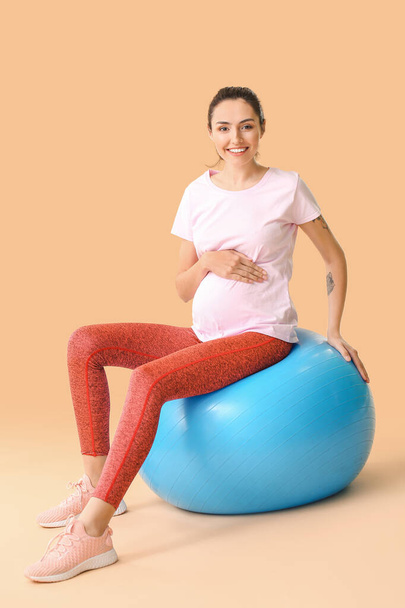 Jovem grávida fazendo exercícios com fitball no fundo de cor
 - Foto, Imagem