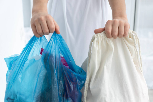 boy holds cotton shopping bag in one hand and blue  plastic bag in other hand, shows difference between natural and polluting material, stop pollution concept - Photo, Image