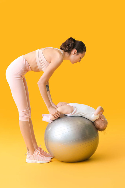Young sporty mother and her baby doing exercises with fitball on color background - Photo, Image