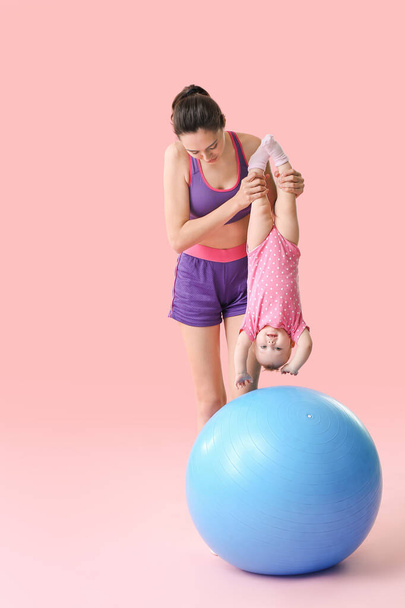 Joven madre deportiva y su bebé haciendo ejercicios con fitball sobre fondo de color
 - Foto, imagen