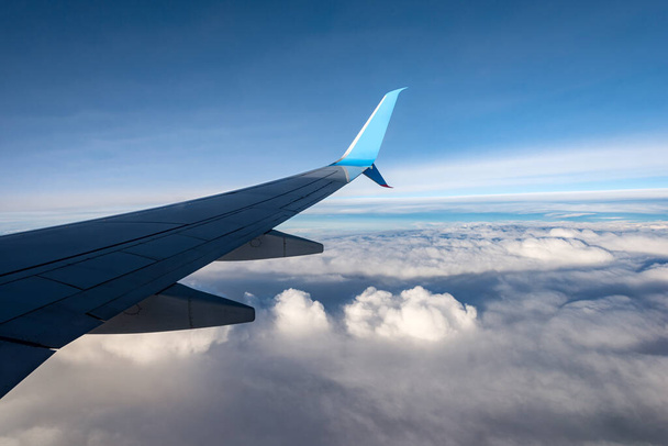 Коммерческий самолет во время полета над облаками. Вид крыла самолета через окно
 - Фото, изображение