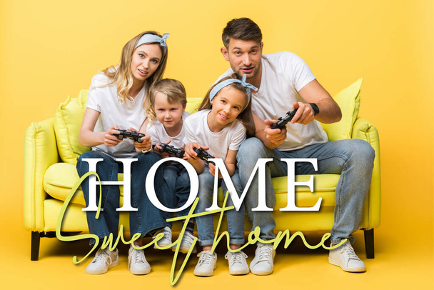 KYIV, UKRAINE - MARCH 4, 2020: cheerful family playing video game with joysticks while sitting on sofa on yellow, home sweet home illustration - Foto, Imagen