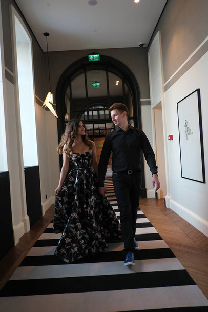 beautiful couple-a girl in a magnificent dress and a guy in a black shirt and trousers are in a building with a beautiful interior - Foto, imagen