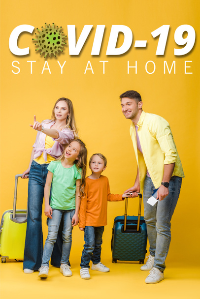glückliche Familie von Reisenden mit Gepäck, Pässen und Eintrittskarten, die auf gelbe, covid-19 Abbildung zeigen - Foto, Bild