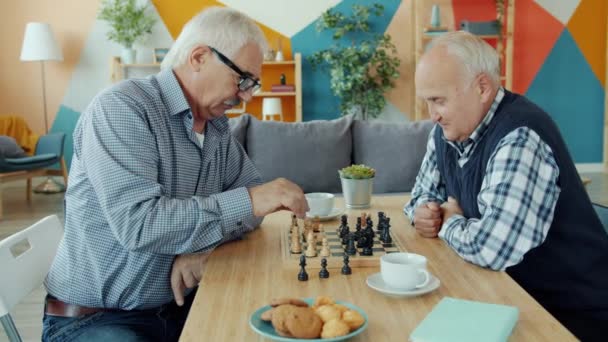 Slow motion of male friends playing chess and talking indoors in apartment - Materiał filmowy, wideo