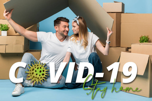 happy couple holding carton roof over heads while sitting on blue with cardboard boxes for relocation, covid-19 illustration - Foto, Bild