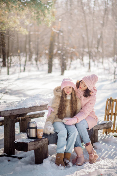 Cute curly girl of 10 years old and her young mother play in the snowy forest in winter - Zdjęcie, obraz