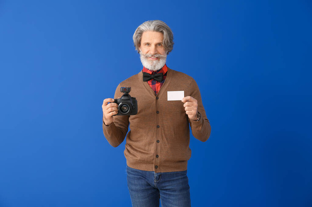 Knappe senior fotograaf met visitekaartje op kleur achtergrond - Foto, afbeelding
