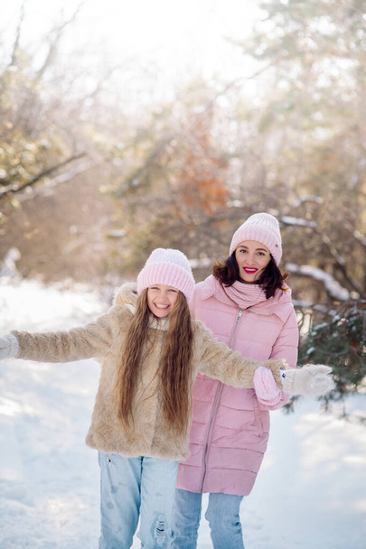 Cute curly girl of 10 years old and her young mother play in the snowy forest in winter - Photo, Image