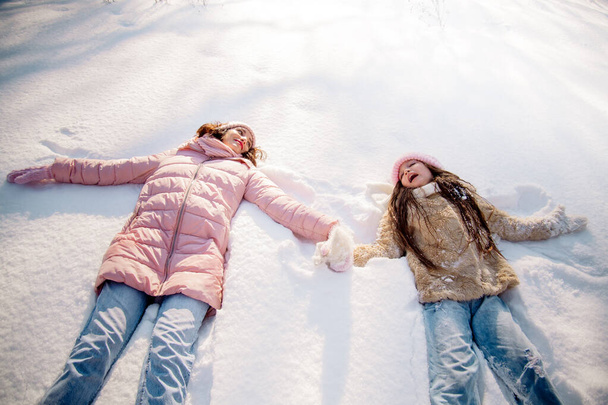 Cute curly girl of 10 years old and her young mother play in the snowy forest in winter - Foto, immagini