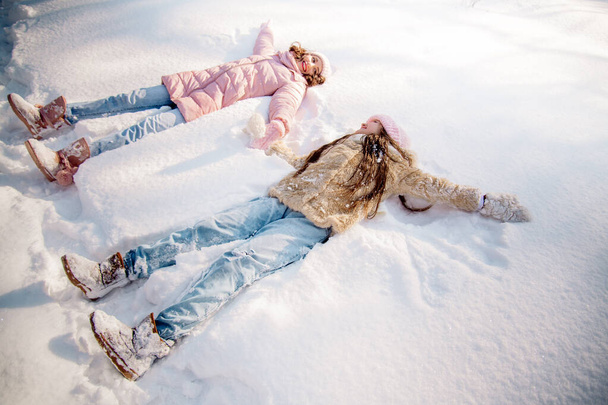 Cute curly girl of 10 years old and her young mother play in the snowy forest in winter - Photo, image