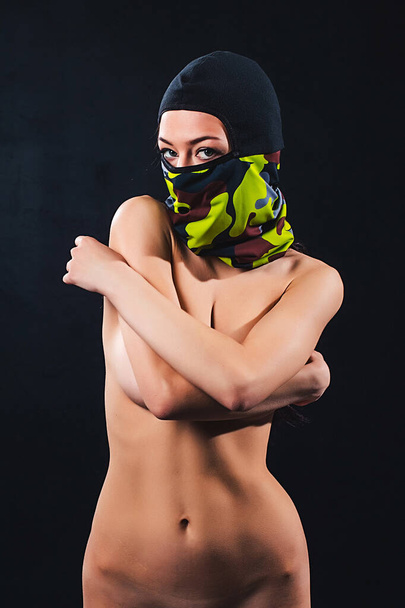 young beautiful girl with make-up, long hair, naked with a good body and forms, on it ski accessories, colored glasses, masks and gloves, shot in the studio on a black background - Photo, Image