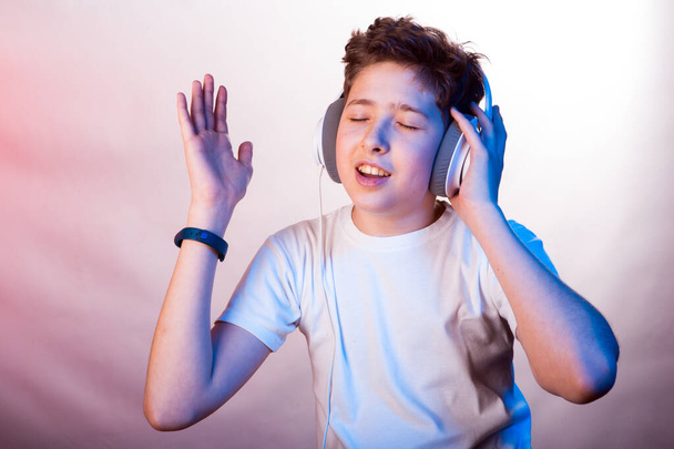 Emotionen und Freude eines jungen Mannes beim Hören seiner Lieblingsmusik. Foto eines jungen Mannes in einem weißen T-Shirt auf einem Hintergrund aus verschiedenen hellvioletten Farbtönen - Foto, Bild