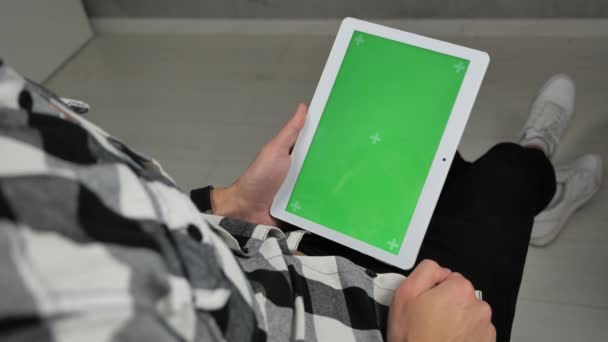 Mężczyzna siedzi na krześle patrząc na cyfrowy tablet z zielonym ekranem chroma key - Materiał filmowy, wideo