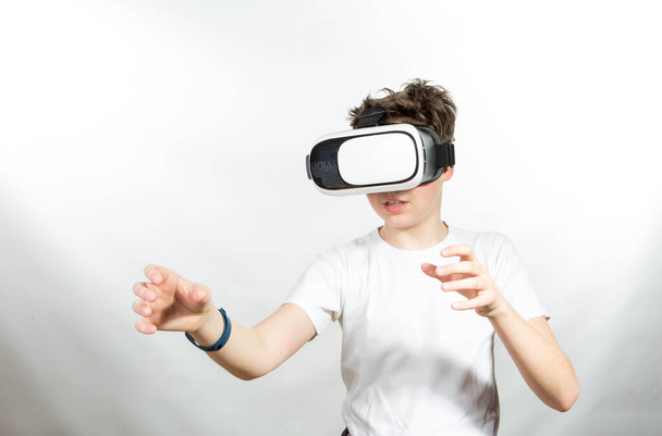 Joyful emotions of a young man when using virtual reality. Photo of a young man in a white T-shirt against a background of prevailing light shades - Photo, image