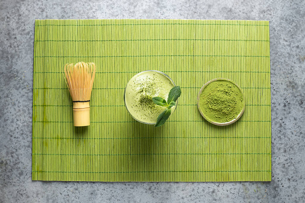 Dalgona Iced Matcha tea, bamboo whisk and matcha powder on green mat. View from above. - Фото, изображение