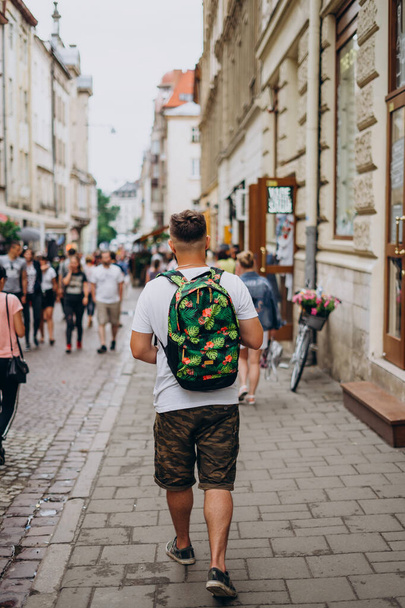 Un hombre con una mochila en un recorrido por la ciudad en el verano. Un joven camina por la ciudad en un día soleado. Tipo deportivo en pantalones cortos y con una mochila de color
 - Foto, imagen