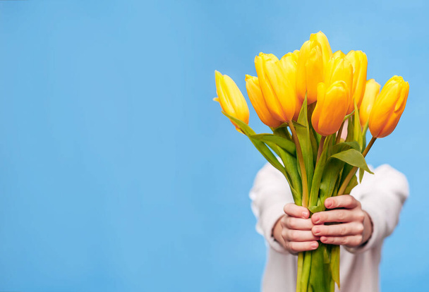 Mały chłopiec na niebieskim tle trzyma w dłoniach bukiet pięknych żółtych tulipanów. Koncepcja święta jest 8 marca, Międzynarodowy Dzień Kobiet, Dzień Matki. Baner, miejsce na tekst. - Zdjęcie, obraz