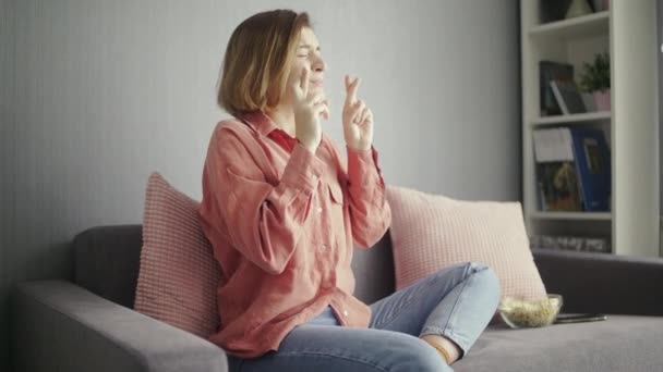 Young worried woman sitting on the sofa and watching TV - Záběry, video