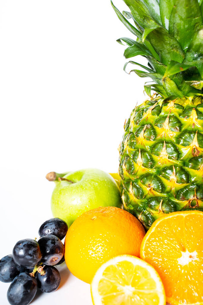 Подборка тропических фруктов на обычном белом фоне, включая весь ананас, зеленое яблоко, банан, апельсин, нарезанный лимон и кучу черного винограда
 - Фото, изображение
